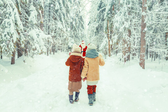 Santa Claus with a bag of gifts and children in a snowy forest.