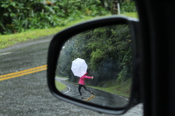 mulher caminhando em estrada com guarda-chuva - vista a partir de retrovisor, na estrada da...