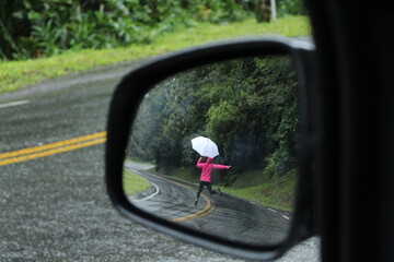 mulher caminhando em estrada com guarda-chuva - vista a partir de retrovisor, na estrada da...