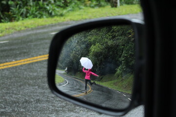 mulher caminhando em estrada com guarda-chuva - vista a partir de retrovisor, na estrada da...