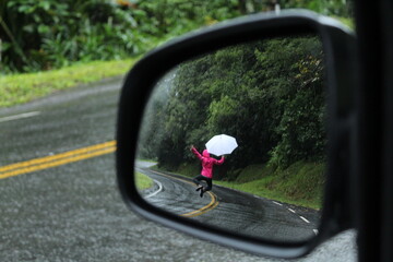 mulher caminhando em estrada com guarda-chuva - vista a partir de retrovisor, na estrada da...