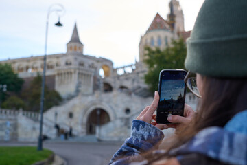 A woman blurred in the background, focused on her phone as she takes a photo of the city
