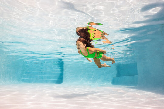 Girl in green swim suit swimming in a pool underwater 