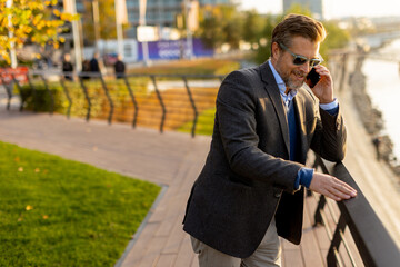 A stylish man enjoys a sunny afternoon while talking on his phone in a vibrant urban setting adorned with fall colors