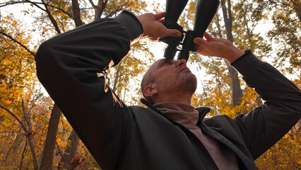 Amateur birdwatcher observing birds and other animals in nature with binoculars.