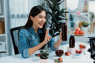 Smiling young beautiful Asian reviewing tasty mixed strawberry and cherry juice detox drinks, showing healthy product to promote for special promotion selling on social media online record. Stratagem.