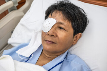 Woman with eye shield lying in hospital bed after doing cataract surgery