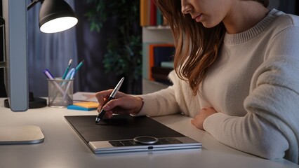 Adult business woman sitting at desk working late at night in office, designer professional using...
