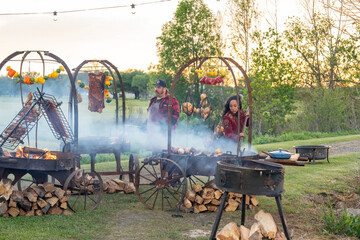 Chefs cooking BBQ and vegetables over open fire in an outdoors setting