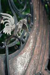 A close-up of intricately detailed metalwork featuring a rooster, symbolizing strength and resilience, against a backdrop of aged iron. The contrast between nature and the industrial world is striking