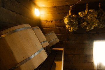 A close-up view of wooden buckets lined up on a shelf in a dimly lit Russian bathhouse. The buckets are made of wood and have metal bands around them.
