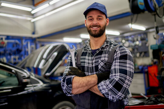 A Caucasian auto mechanic proudly posing in his workshop for a photograph.