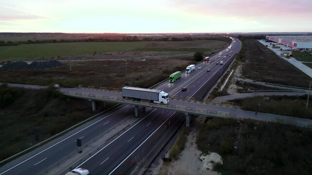 Low-altitude drone view from a newly paved highway overpass overlooking an active motorway during road construction. Modern transportation infrastructure with moving traffic, construction works and ex