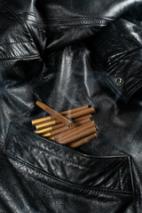 Black leather jacket pocket holding cigarettes with faint smoke trails
