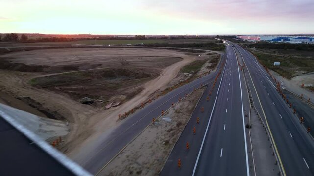 Low-altitude drone view from a newly paved highway overpass overlooking an active motorway during road construction. Modern transportation infrastructure with moving traffic, construction works and ex
