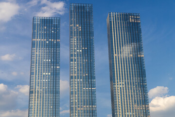Obraz premium A clear view of three modern skyscrapers in Moscow, Russia, reaching towards a bright blue sky with fluffy white clouds.