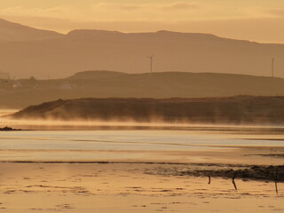Rising sun illuminating mist on the surface of Pool Roag loch on the Isle of Skye, Scotland