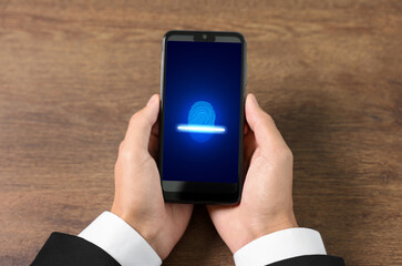 Man holding smartphone with fingerprint scanner at wooden table, closeup