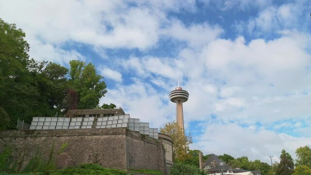 iconic Skylon Tower rises above lush greenery and stone structures under bright blue sky with scattered clouds in Niagara Falls, Canada. Skylon Tower Niagara Falls, Canada blue sky Niagara Falls