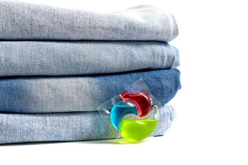 A stack of jeans pants with laundry capsules lie on a white background.	