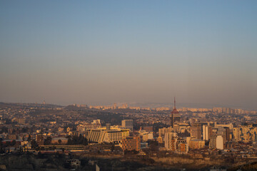 Fototapeta premium The city of Tbilisi glows softly as winter dusk descends, revealing a tranquil urban landscape embraced by nature.