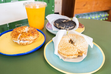 Toasted sesame bagel with cream cheese on plate with orange juice,Fresh baked New York style bagels,london bagel,Three Different Types of Bagels in cafe,baked sourdough,Brunch bakery shop.