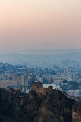 Obraz premium Snow blankets the hills as Tbilisi glimmers under a soft winter sunset, blending history with serene beauty.