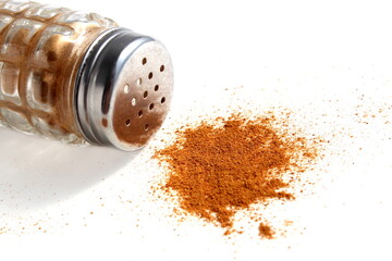 There is a glass salt shaker with red pepper on a white background.