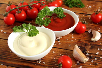 Two bowls of mayonnaise and ketchup stand on a wooden table.	