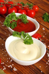 Two bowls of mayonnaise and ketchup stand on a wooden table.	