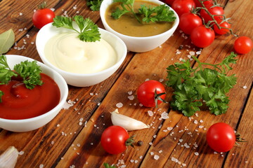 There are three bowls of mayonnaise, ketchup and mustard on a wooden table.	