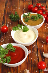 There are three bowls of mayonnaise, ketchup and mustard on a wooden table.	