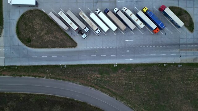 Drone shot of truck parking in Europe seen from above. Aerial footage of rows of vehicles parked for rest at a service station. Neatly placed trucks arranged at a truck stop seen from a helicopter.
