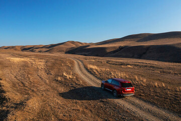 A red car is seen driving down a dusty dirt road in rural Georgia, kicking up clouds of earth behind it.