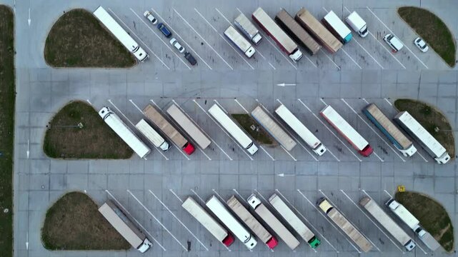Drone shot of truck parking in Europe seen from above. Aerial footage of rows of vehicles parked for rest at a service station. Neatly placed trucks arranged at a truck stop seen from a helicopter.
