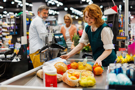 Smiling cashier scanning groceries at supermarket checkout