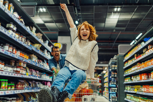 Happy couple having fun riding shopping cart in supermarket