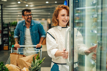 Happy couple shopping for groceries, opening refrigerator in supermarket