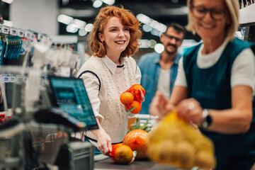 Young woman placing oranges on checkout counter in supermarket