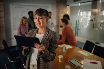 Smiling businesswoman holding tablet, leading meeting in modern office