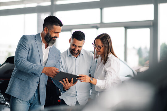 Professional car dealer advising satisfied couple in showroom.
