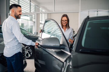 Salesman introduces woman to new vehicle in showroom setting.