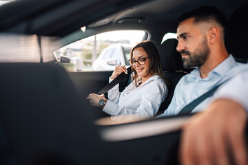 Woman fastening seatbelt in car, smiling at driving companion