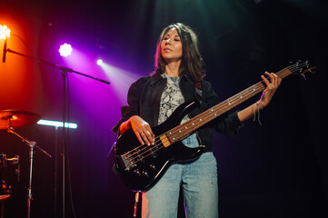 Obraz premium Female musician playing bass guitar on stage under colorful lights