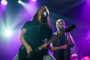 Guitarist performing with passion on stage under purple lights
