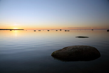 Peaceful seascape at sunset with smooth water, scattered rocks, and a colorful gradient sky. Perfect serene nature background for relaxation or meditation themes.