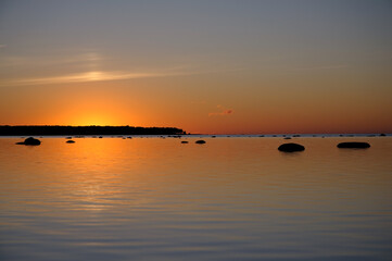 A vibrant sunset over calm water with scattered rocks and a glowing orange horizon, creating a tranquil and picturesque seascape. Ideal for serene and peaceful themes.