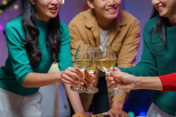 Group of friends toasting with glasses of white wine, celebrating christmas holidays together at home