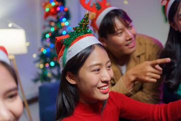 Group of young friends wearing christmas hats enjoying christmas party, playing games and having fun at home