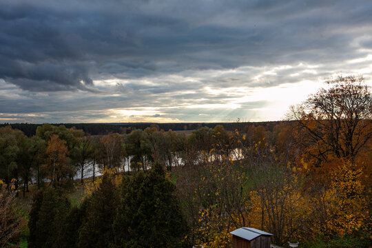 Panoramic view of Arkhangelskoe Estate in Russia, with stunning autumn foliage, a winding river, and a mix of dark clouds and sunbeams in the sky.